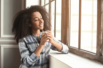 Beautiful African-American woman drinking coffee near window