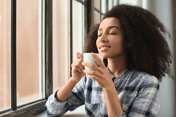 Beautiful African-American woman drinking coffee near window