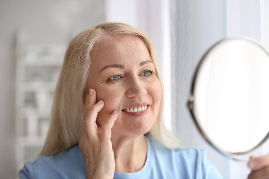 Mature Woman With Healthy Skin Looking In Mirror At Home