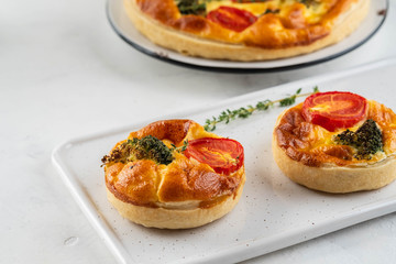 Vegetable pie quiche with broccoli, tomatoes and soft cheese on white background.