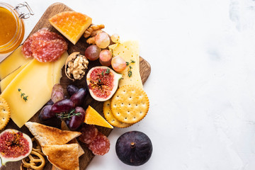 Cheese plate served with grapes, jam, figs, crackers and nuts on a background.