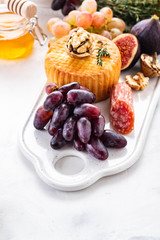 Cheese plate served with grapes, jam, figs, crackers and nuts on a background.