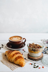 Delicious breakfast on the table. The cup of coffee, mango chia pudding and croissant at the white...