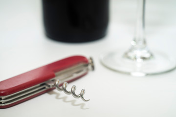 Folding knife with wine opener, glass and wine bottle on a white background