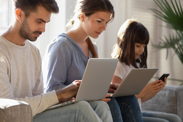 Family sitting on couch absorbed in digital devices