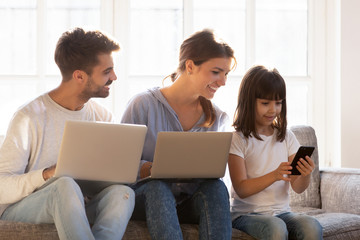 Smiling family sitting on couch absorbed in digital devices