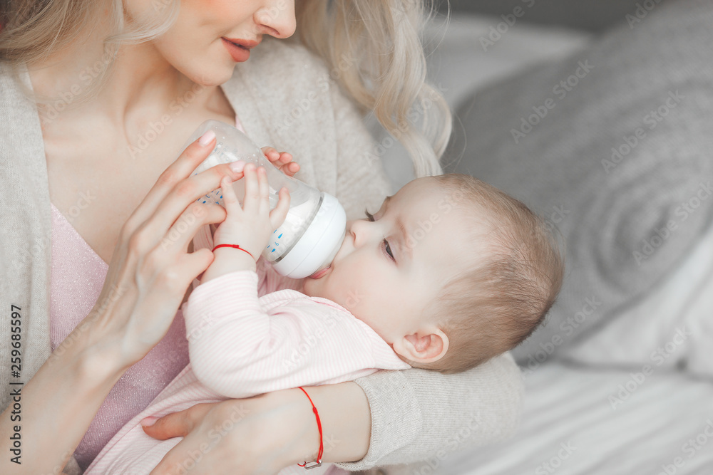 Wall mural little cute baby sucking the bottle with formula. mothe feeding her little child with breast milk.