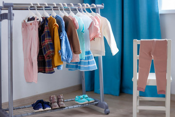 Children's cloth rack, selective focus. Pastel color children's  clothes in a Row on Open Hanger indoors. Clothes for little ladies hung in the children's room. Turquoise and pastel pink colors.