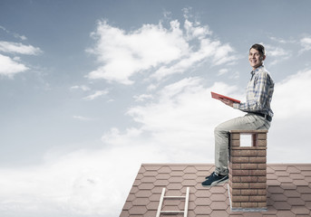 Handsome man on brick roof against cloud scape reading book