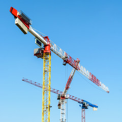 Low angle view of three large tower cranes on a construction site against blue sky.