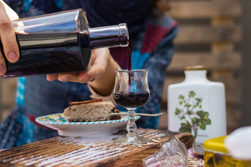 Woman hands holds and pours deep red color liquor drink in shot glass and beautiful decanter on served table. is Alcoholic hard drink fermented with sugar.