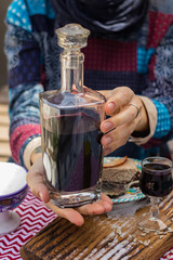 Woman hands holds deep red color liquor drink in shot glass and beautiful decanter on served table. is Alcoholic hard drink fermented with sugar.