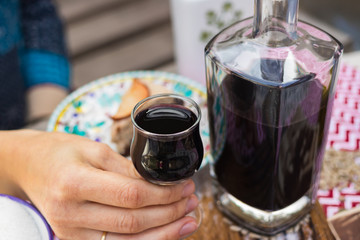 Woman hands holds deep red color liquor drink in shot glass and beautiful decanter on served table. is Alcoholic hard drink fermented with sugar.