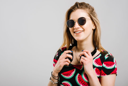 Young caucasian woman in sunglasses with headphones posing on grey background