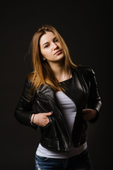 Fototapeta premium Young caucasian woman wearing a leather jacket and jeans posing on the black background