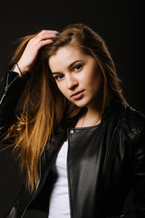 Fototapeta na wymiar Young caucasian woman wearing a leather jacket and jeans posing on the black background