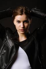 Young caucasian woman wearing a leather jacket and jeans posing on the black background