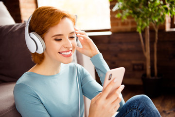 Close up photo beautiful she her lady hands telephone smart phone earflaps check choose audio track wear blue pullover jeans denim clothes sit floor fluffy carpet divan house loft living room indoors