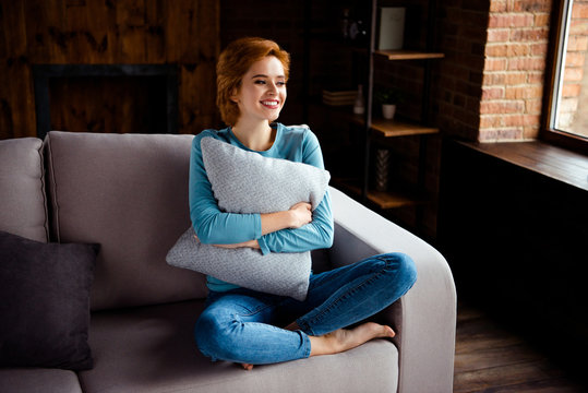 Close up photo beautiful she her lady hands arms hug embrace pillow red short hairdo look window imaginary flight wear blue pullover jeans denim clothes sit comfort divan house living room indoors