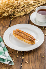 Homemade eclair dessert with chocolate sauce and cup of tea on wooden table