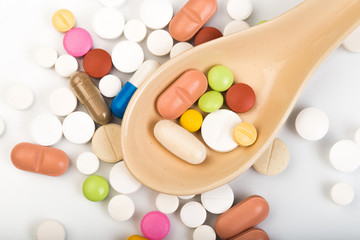 Colorful medical pills on spoon and capsules or supplements for therapy in background, concept of treatment and health care