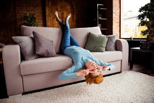 Full length body size photo beautiful she her lady hands arms legs raised upside down show v-sign eyes best day wear blue casual pullover jeans denim sit comfy couch divan house living room indoors