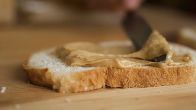 Delicious and hearty breakfast nut cream on a crisp bread. Man makes a peanut butter sandwich.. Closeup of male hands spreading butter on bread in kitchen,  slow motion.