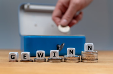 Symbol für steigende Gewinne. Würfel bilden das Wort "Gewinn". Würfel stehen auf Münzstapeln vor einer Geldkassette.