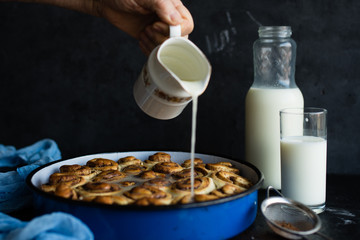 Baker drizzling glaze over cinnamon rolls