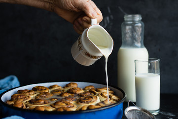 Baker drizzling glaze over cinnamon rolls