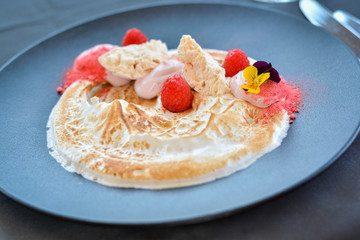 White cream desert with raspberries on black plate in restaurant.