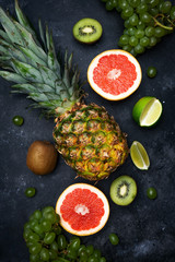 Tropical fruits background. Pineapple, grapefruit, kiwi, grapes, lime on a dark background. Summer, health, vitamins, vegan concept.