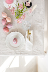 Beautiful festive Easter table setting with linen tablecloth, painted eggs and flowers