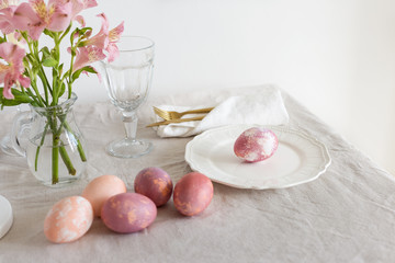 Easter serving plate with pink Easter eggs, gold tableware, glass and flowers on linen tablecloth in the morning