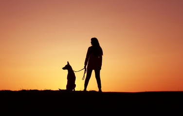 Silhouettes at sunset, girl and dog against the backdrop of an incredible sunset, Belgian Shepherd dog Malinois