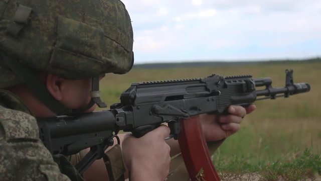 Russian soldier in armor and helmet firing a machine gun. Soldier shoots AK 74m