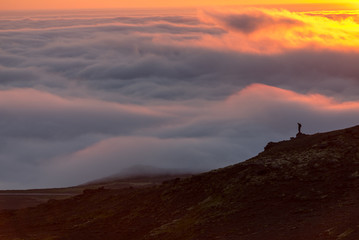 Silhouette of a man on the ridge above the sea of clouds, misty mountains at sunset in Iceland