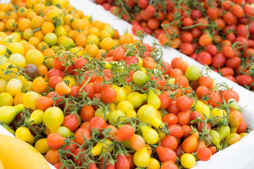 Detail on a market stall of fresh tomatoes, with focus on orange cherry tomatoes in the foreground. Organic food concept.