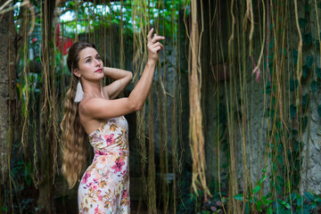 Beautiful young woman is leaning against a tree in the rain forest wearing sexy dress