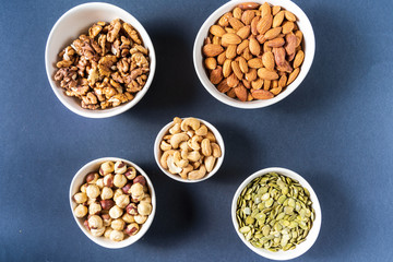 Obraz na płótnie Canvas Variation of nuts in bowls on gray background.