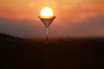 Fototapeta premium Silhouette of martini glass on sunset background, setting sun in a glass