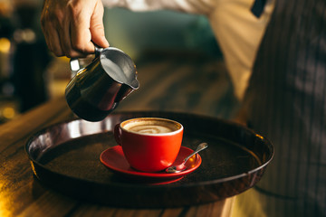 waiter pouring milk into cup of coffee