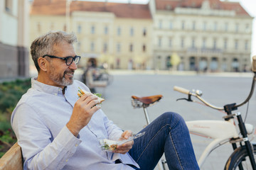 senior man eating sandwiches outdoor in the city