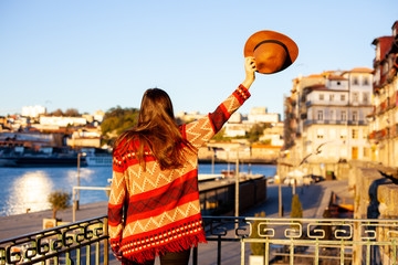 Young woman with long hair walking on city street at sunrise, wearing hat and coat, enjoying happy pleasant moment of her vacations