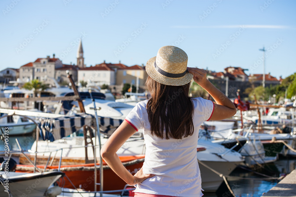 Wall mural Beautiful young woman in hat standing close to the boats at Mediterranean city marina port.