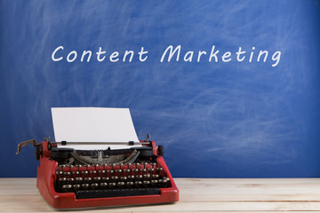 writer's workplace - red typewriter on blue blackboard background with text "content marketing"