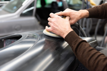 Professioneller Autolackierer schleift ein Autoteil mit der Schleifmaschine vor in einer Werkstatt - Serie Autowerkstatt