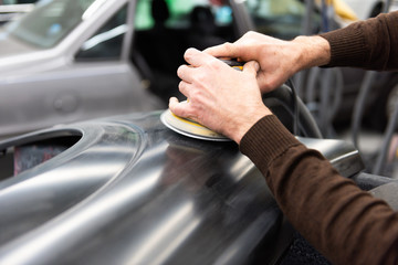 Professioneller Autolackierer schleift ein Autoteil mit der Schleifmaschine vor in einer Werkstatt - Serie Autowerkstatt