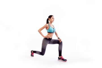 Fototapeta premium A dark-haired woman coach in a sporty short top and gym leggings makes lunges by the feet forward, hands are held out to the side on a white isolated background in studio