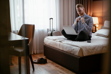 Man working on his laptop. Executive manager talking on the phone while working on his laptop. Businessman sitting on the bed working.